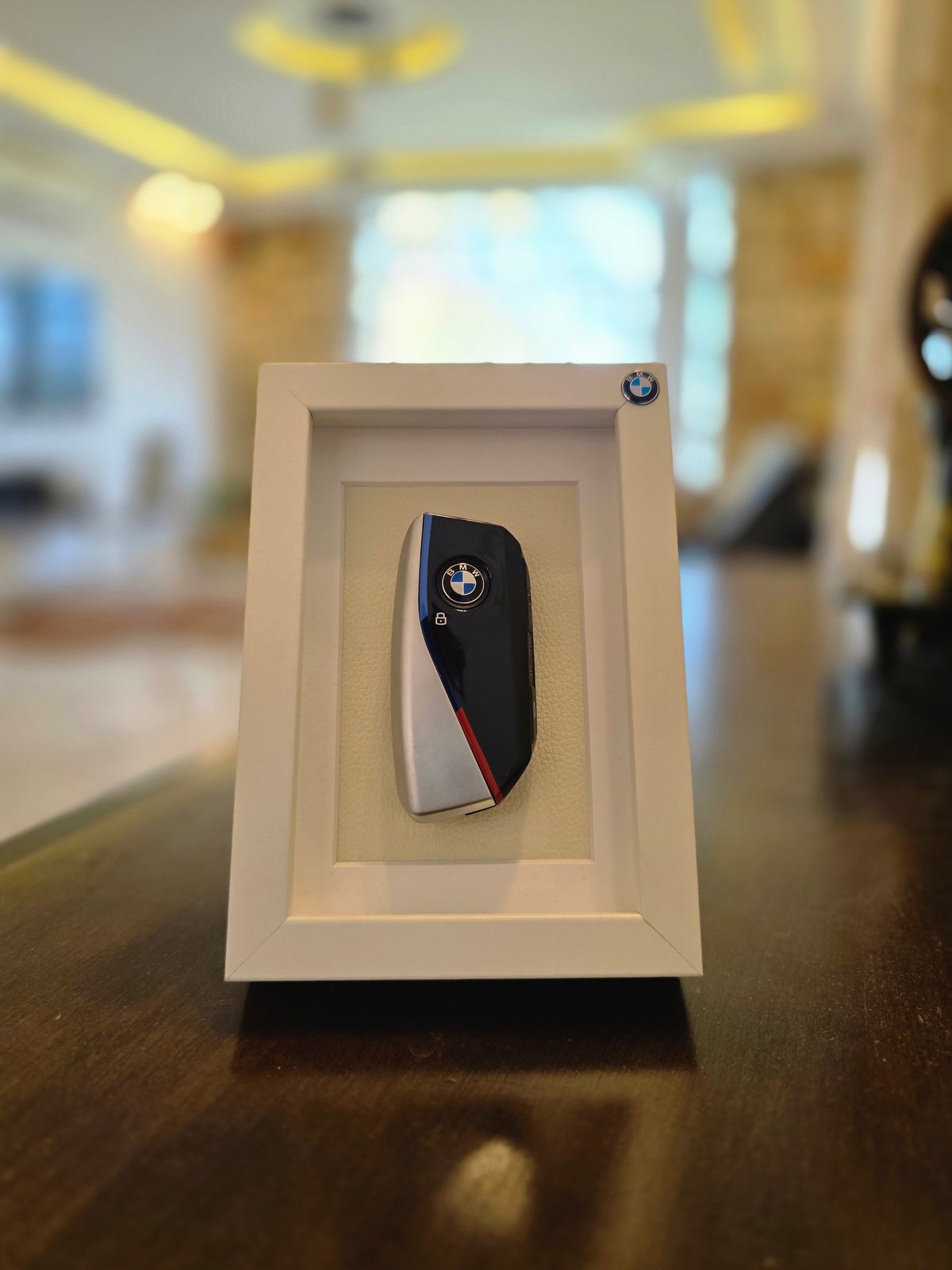 Decorative wall art with a BMW logo in a beige frame on a wooden surface.