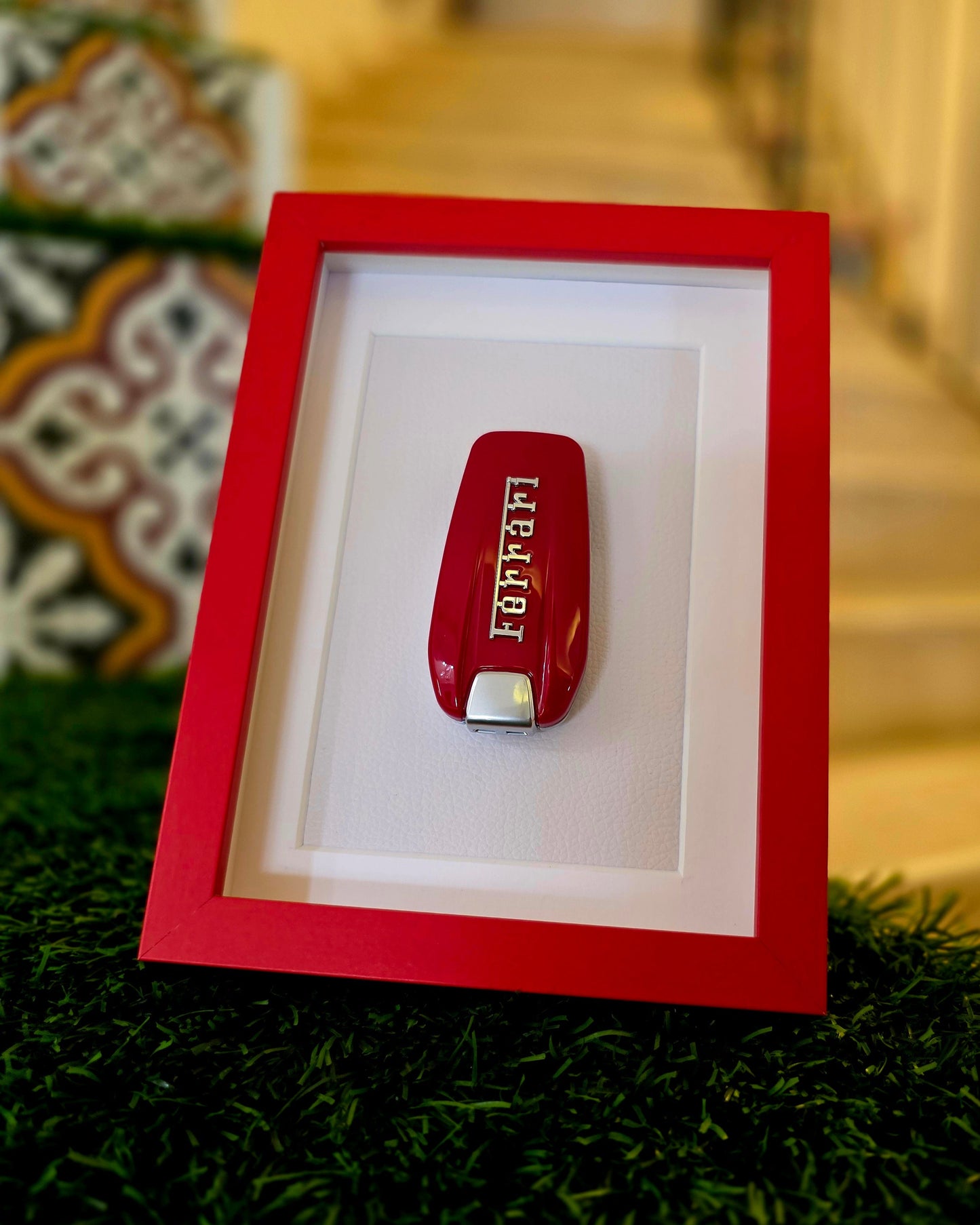 Red Ferrari pocket knife in a red frame on a grassy surface with a blurred decorative background.