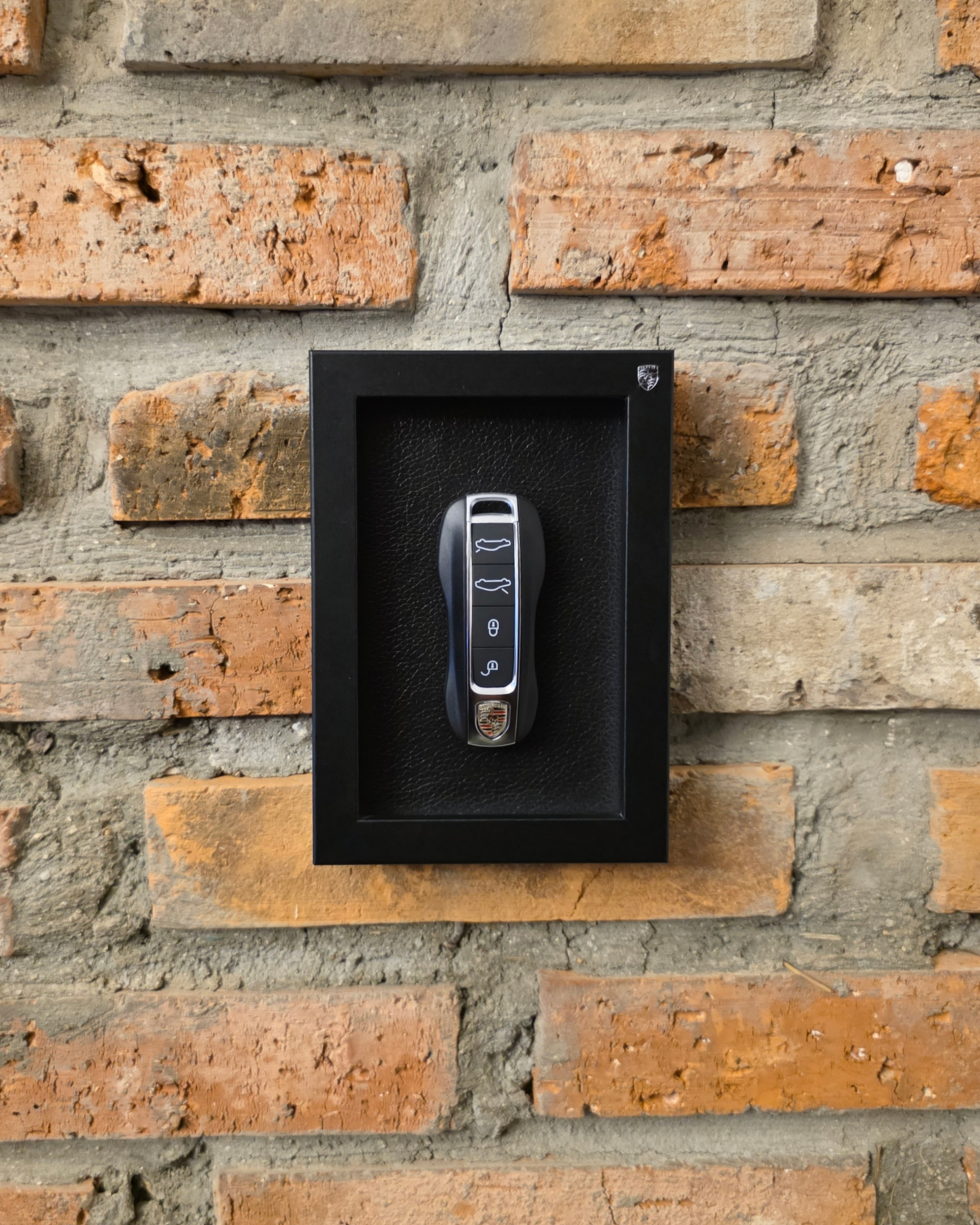 porsche key in a black frame on a brick wall
