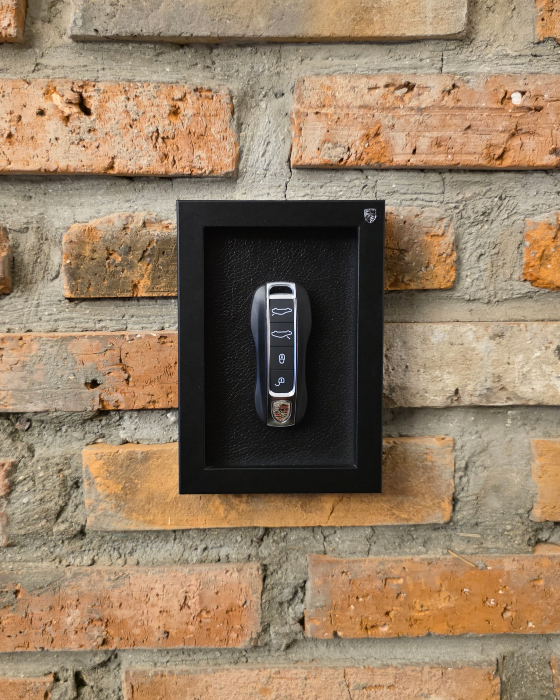 porsche key in a black frame on a brick wall