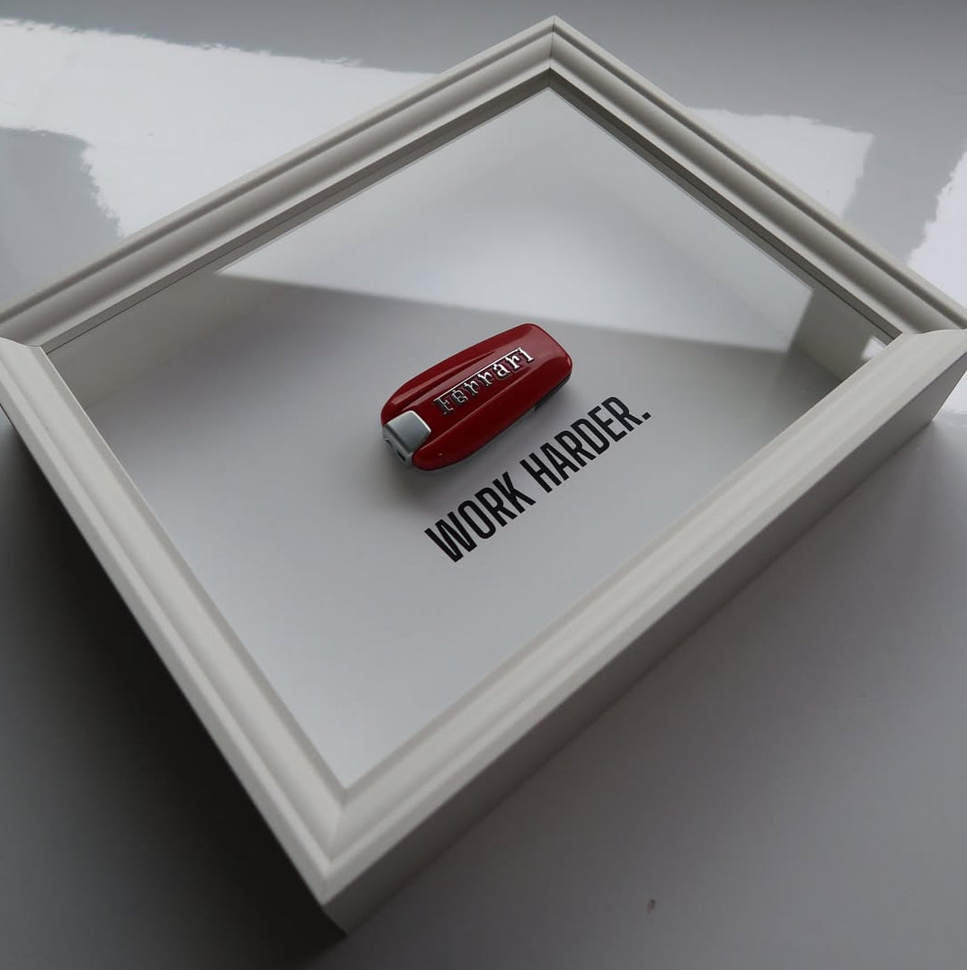 Red ferrari key with 'WORK HARDER' text in a white frame