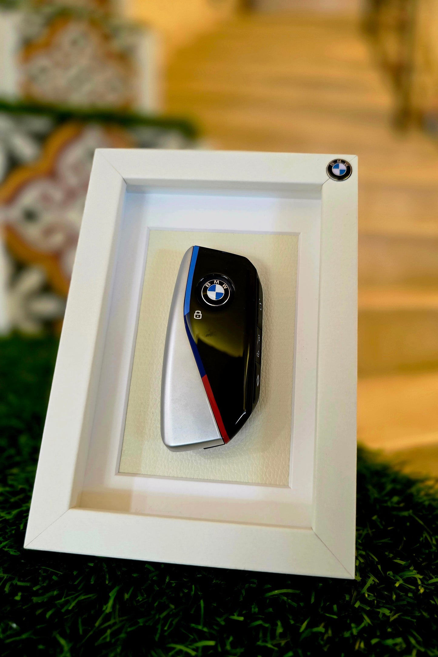 BMW key fob in a white frame on a grassy surface with blurred background