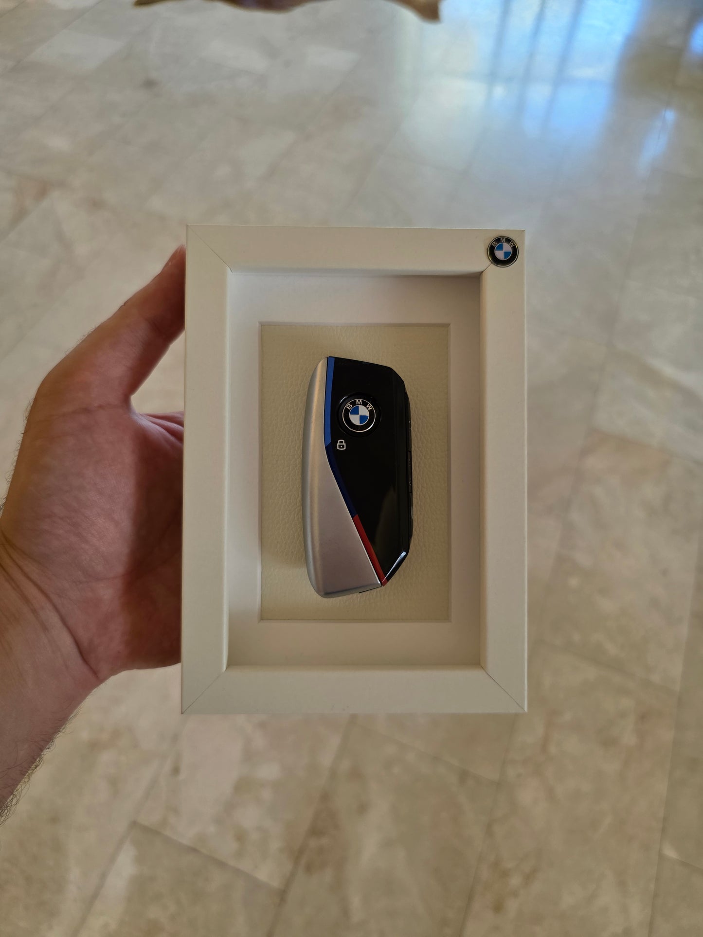 BMW logo in a white frame held by a hand on a marble surface